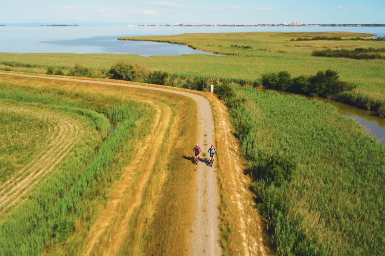 Een onverhard pad met twee fietsers, omringd door velden en een waterpartij.
