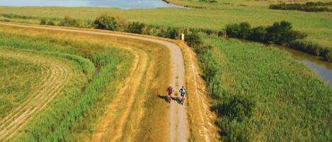 Een onverhard pad met twee fietsers, omringd door velden en een waterpartij.