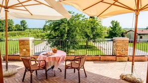 A patio with a table and chairs, a view of a green landscape, and a brick wall.