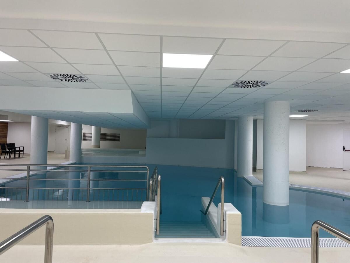 A large indoor swimming pool with a central staircase, surrounded by columns and a tiled floor.