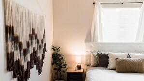 Un dormitorio con cama, mesita de noche, lámpara y un cuadro en la pared.