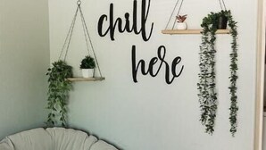 Una habitación con un cartel en la pared que dice "chill here", una planta colgante y un sillón de girable.
