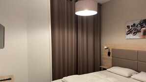 A hotel room with a bed, a bedside table, a lamp, a painting on the wall, and a curtain.
