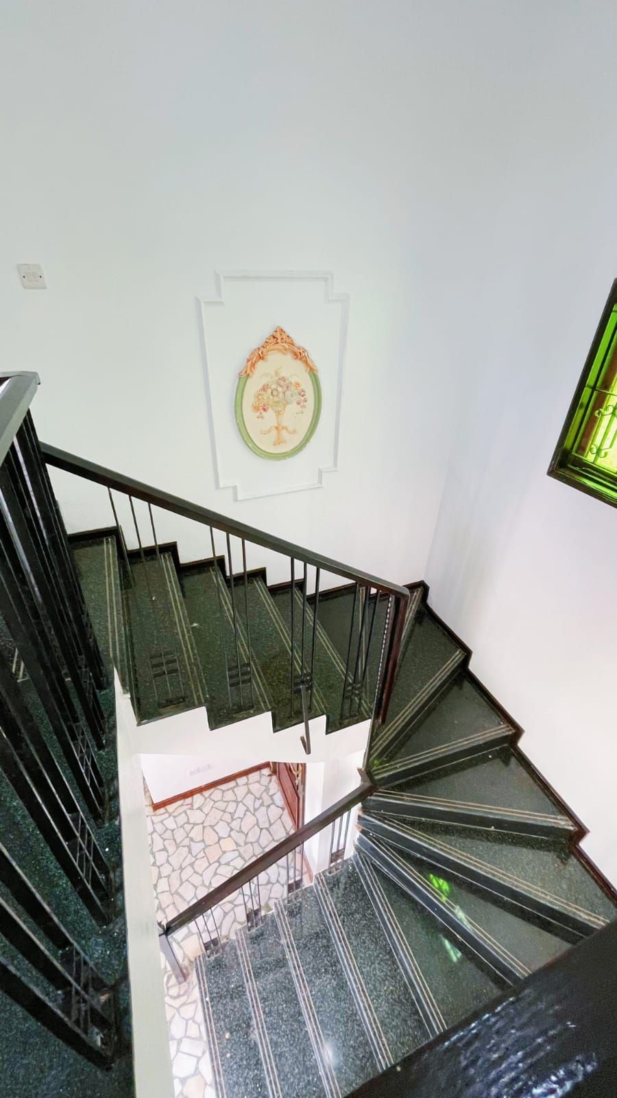 A staircase with a handrail, a wall-mounted picture, and a window with a green frame.