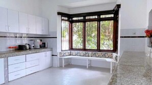 Une cuisine spacieuse avec des meubles blancs, un plan de travail en granit et une grande fenêtre donnant sur un paysage verdoyant.