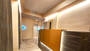 A hotel reception area with a wooden reception desk, a wooden floor, and a door in the background.