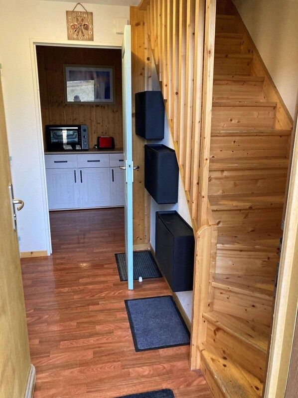Un pasillo estrecho con suelo de madera, un microondas, armarios y una escalera de madera.