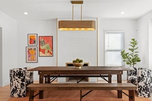 A dining area with a wooden table, two chairs, a bowl of fruit, and framed artwork on the wall. - Spacious Detroit Retreat • Sleeps 16 • Parking (Detroit)