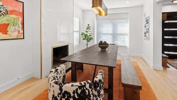 Uma área de refeições moderna com uma mesa de madeira, cadeiras estampadas em preto e branco, um banco e uma luminária pendente.