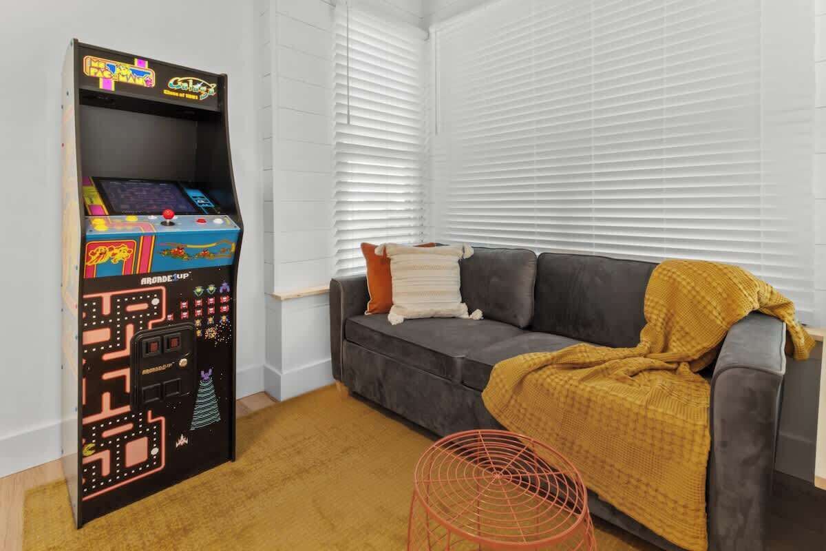 A room with a sofa, a blanket, a small table, and a retro arcade game.