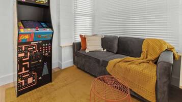 A room with a sofa, a blanket, a small table, and a retro arcade game.