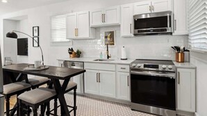 A modern kitchen with white cabinets, a stainless steel microwave, and an oven. - Spacious Detroit Retreat • Sleeps 16 • Parking (Detroit)