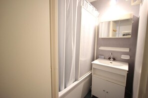 Une petite salle de bain avec un lavabo blanc, un miroir et un rideau de douche.