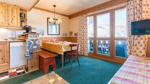 Une cuisine chaleureuse avec des meubles en bois, une table à manger et une vue sur l’extérieur grâce à de grandes fenêtres.