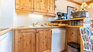 Une cuisine avec des meubles de rangement en bois, un lave-vaisselle, une machine à café et un luminaire suspendu.