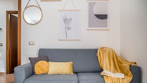 A grey sofa with a yellow throw blanket and a book, a round mirror, and framed artwork on the wall.