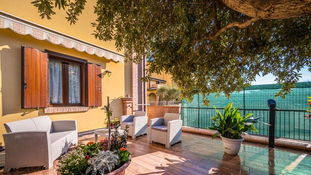 A balcony with wicker furniture, potted plants, and a view of the sea.