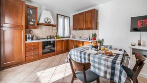 A modern kitchen with wooden cabinets, a dining table with a checkered tablecloth, and a flat-screen TV mounted on the wall.
