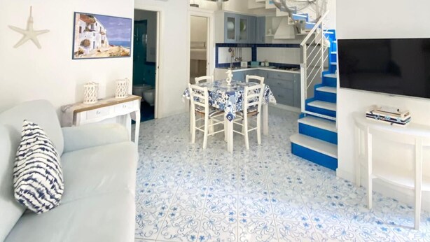 A living room with a sofa, a dining table, and a kitchen area with blue stairs. - Arime Apartment
Elegance and Tradition a Stone's Throw from the Sea" (Lacco Ameno)