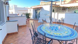 A covered patio with a round table and chairs, a potted plant, and a view of neighboring buildings. - Arime Apartment
Elegance and Tradition a Stone's Throw from the Sea" (Lacco Ameno)