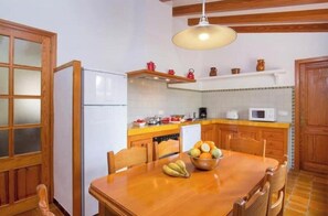 A kitchen with wooden cabinets, a white refrigerator, a microwave, and a dining table with fruit.