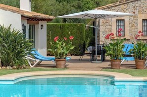 A swimming pool with lounge chairs, potted plants, and a stone building in the background.