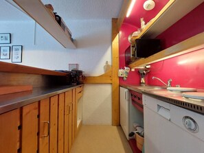 A compact kitchen with wooden cabinets, a white stove, and a red backsplash.