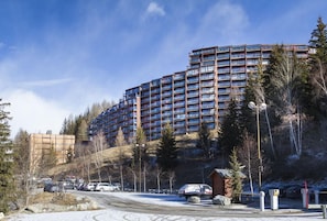 A multi-story hotel with a modern architectural design, located in a hilly area with trees and a parking lot.