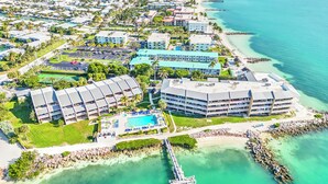 An aerial view of a coastal resort with multiple buildings, a swimming pool, and a pier extending into the water. - Fresh & Light Oceanfront Condo (Key Colony Beach)