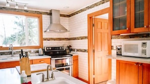 A modern kitchen with white tiles, a stainless steel range hood, a built-in oven, and a microwave.