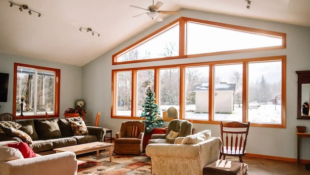 A spacious living room with large windows, a ceiling fan, and a Christmas tree.