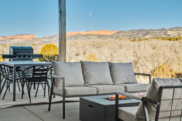 An outdoor patio with a gray sofa, black chairs, a table, and a grill.