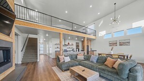 A spacious living area with a large sectional sofa, a wooden coffee table, and a staircase leading to an upper level. - The Grove-River Cabin -Hot Tub- Family Home Near Bryce & Zion (Hatch)