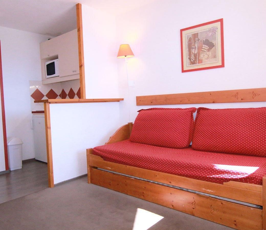 A small, cozy room with a wooden bed, a white wall, a framed picture, and a small white cabinet.