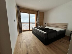 Een slaapkamer met een groot bed, een glazen schuifdeur naar een balkon en houten vloeren.