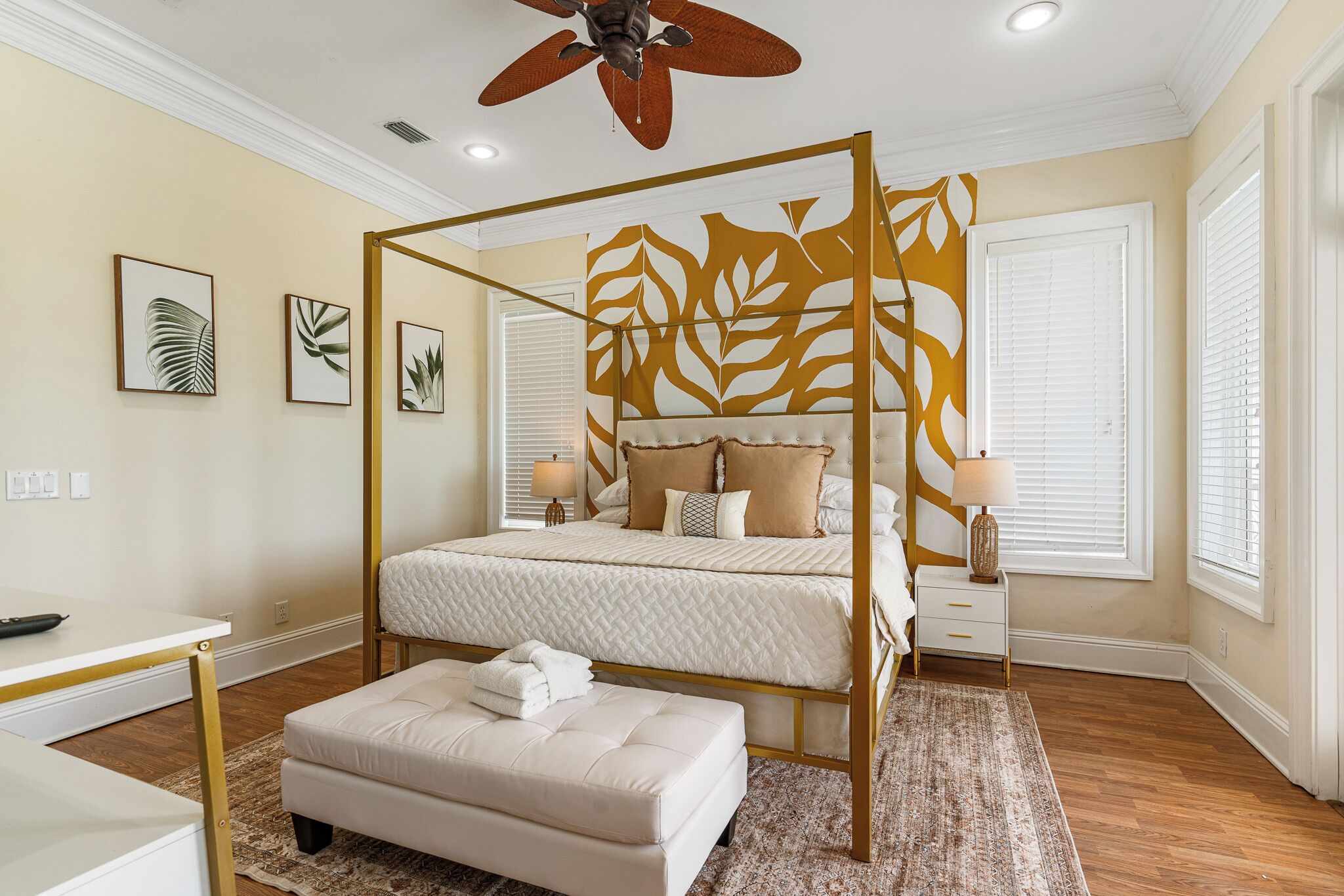 A four-poster bed with a leaf-patterned headboard, a bedside table with a lamp, and a small bedside drawer.