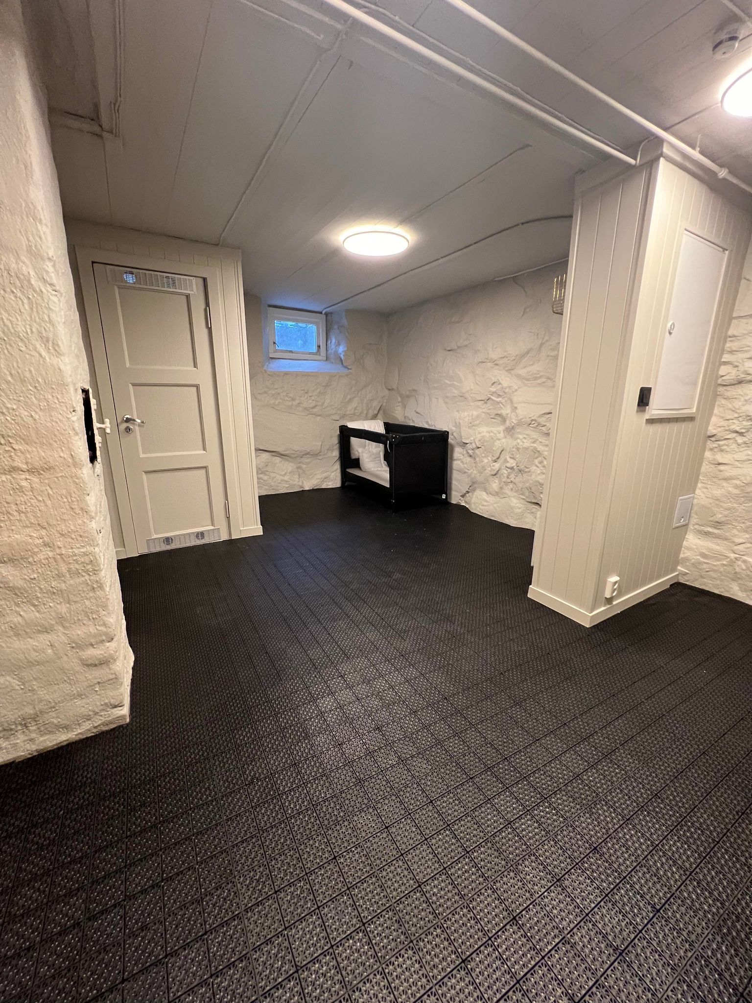 A room with a dark patterned floor, white walls, a small window, and a door.