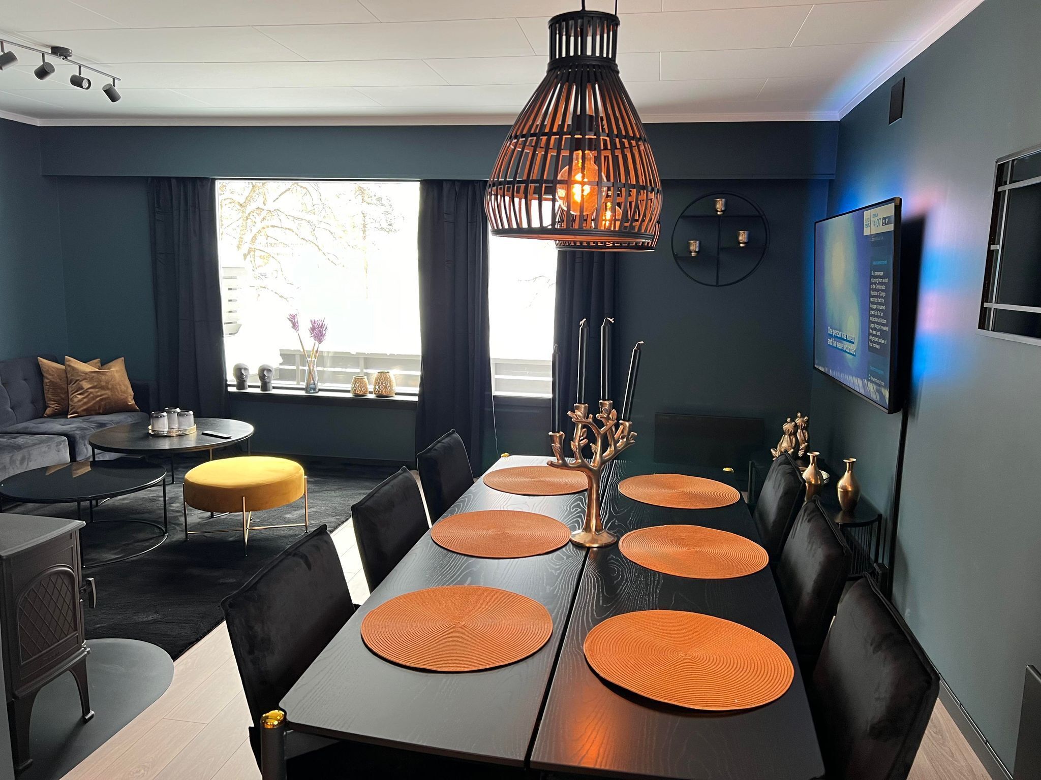 Un comedor moderno con una mesa larga, sillas negras y posavasos anaranjados.