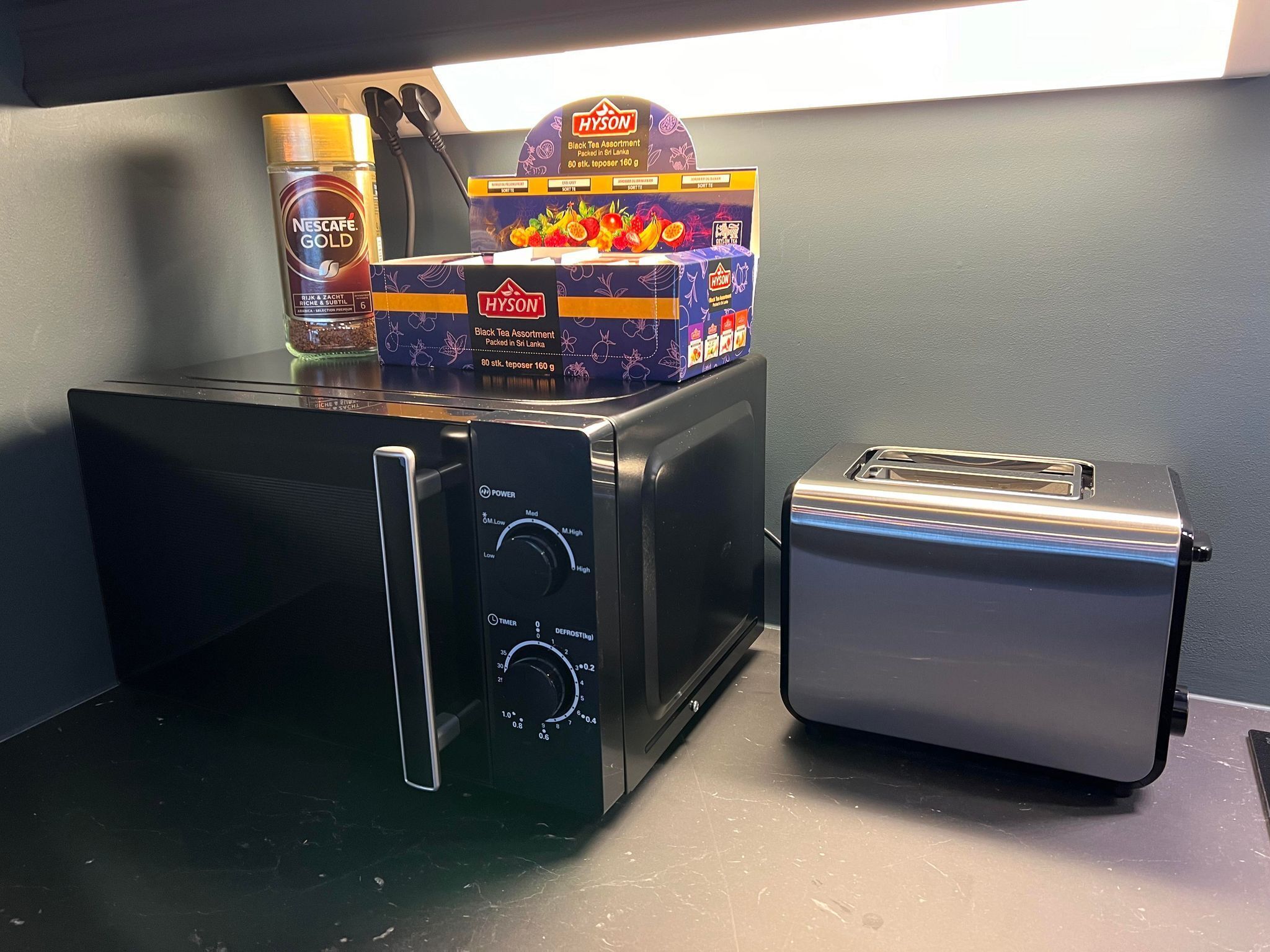 A kitchen with a microwave, toaster, and a box of black tea.