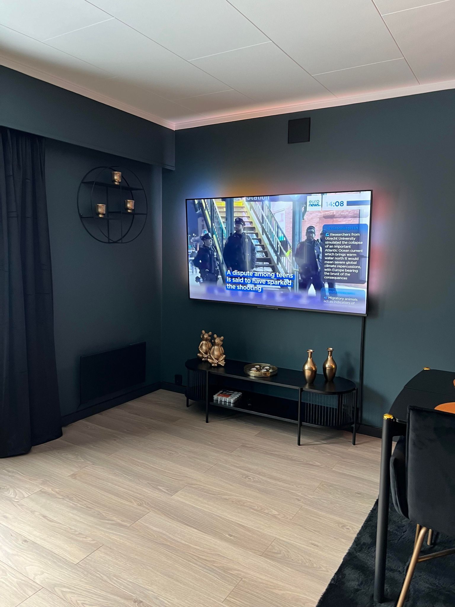 Un salon moderne avec un grand téléviseur à écran plat fixé au mur, un meuble de rangement noir en dessous et un rideau bleu foncé sur le côté gauche.