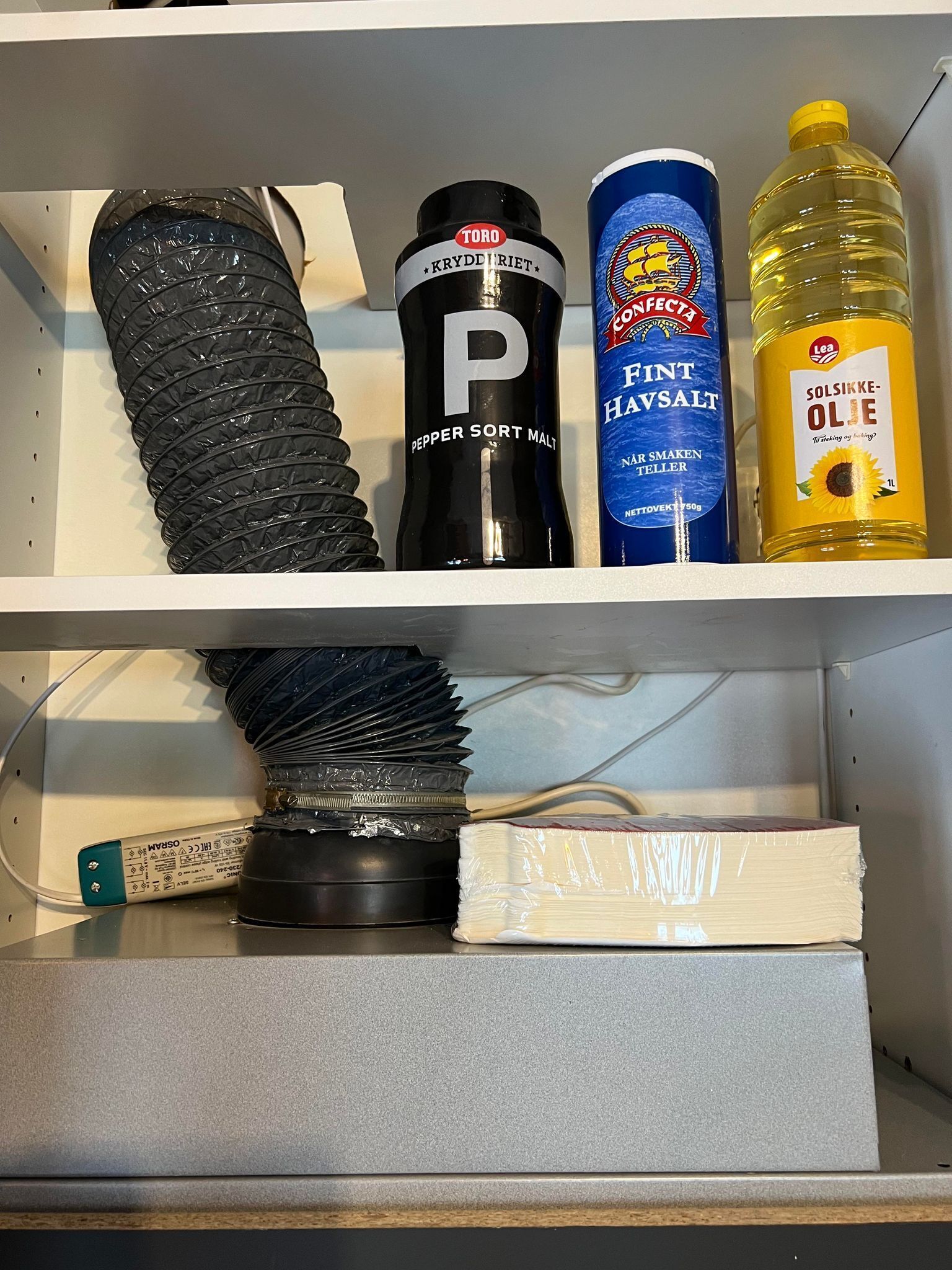 A shelf with a black pepper sort malt, a blue can of mint hawsalt, a yellow bottle of soliskke-olie, and a black coiled hose.