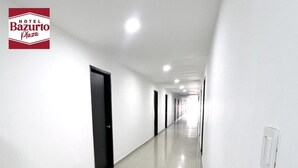 Un largo y estrecho pasillo de hotel con paredes blancas y piso de baldosas.