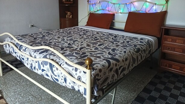 A bed with a patterned bedspread, a headboard with lights, and a nightstand with drawers.