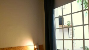 Een hotelkamer met een bed, een raam met gordijnen en een aan de muur bevestigde lamp.