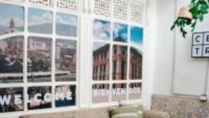 Een woonkamer met een beige bank, een glazen salontafel en een muur versierd met ingelijste foto's en een bord met een welkomstboodschap.