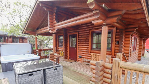 A log cabin with a hot tub, wicker furniture, and a wooden deck. - 24 Lakeside Drive (Morpeth)