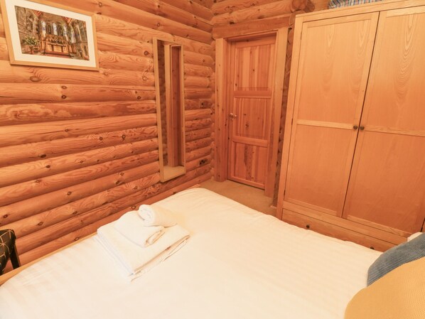 A log cabin bedroom with a bed, a wooden wardrobe, and a door.