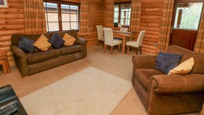 A log cabin interior with a sofa, a dining table with chairs, and a TV stand. - 24 Lakeside Drive (Morpeth)