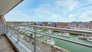 A balcony with a view of a marina, boats, and buildings in the background. - Un Balcon sur le Port - Place de parking (Courseulles-sur-Mer)