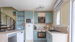 A compact kitchen with a microwave, oven, and dishwasher, a small sink, and a staircase leading to another room. - Un Balcon sur le Port - Place de parking (Courseulles-sur-Mer)